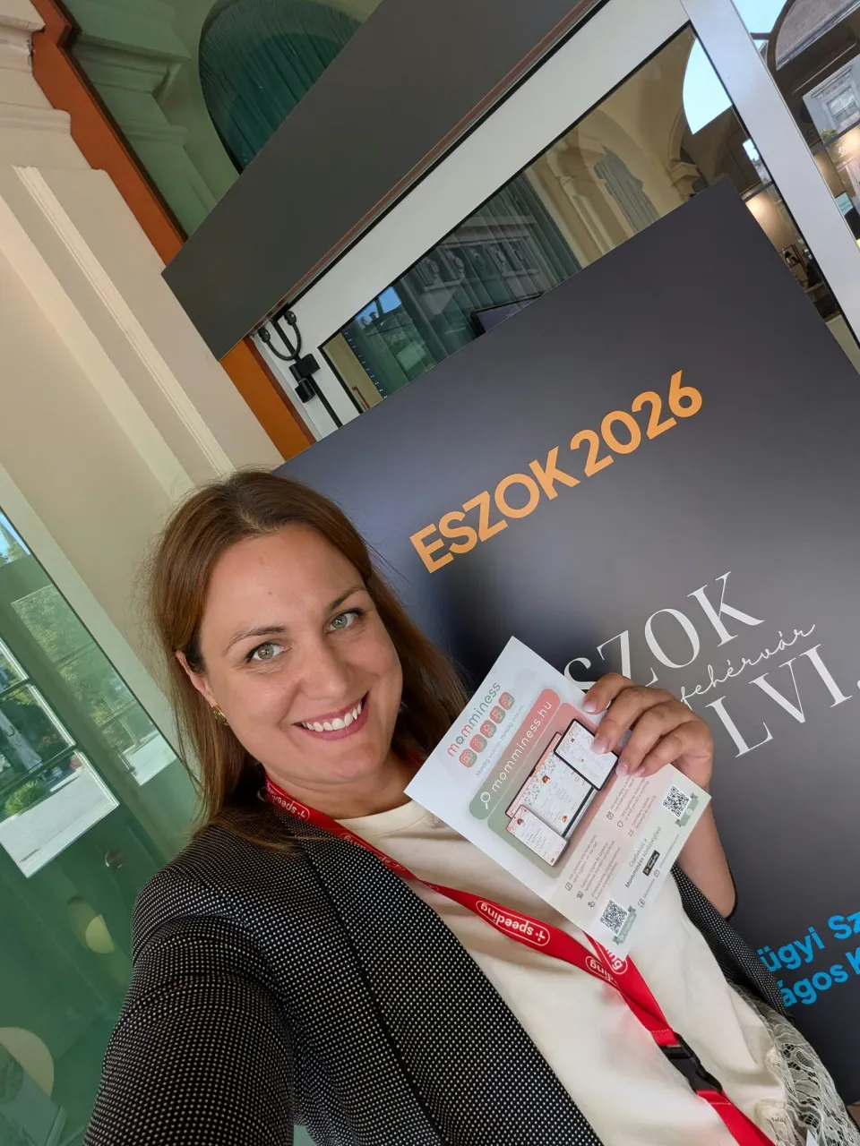 Zsebe-Vasvári Viktória holds a Momminess leaflet beside the ESZOK 2026 display in Székesfehérvár.