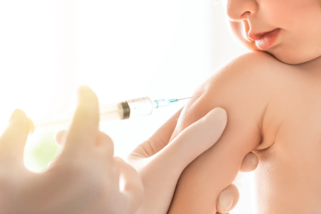 A healthcare professional administers a vaccine to a baby’s upper arm.